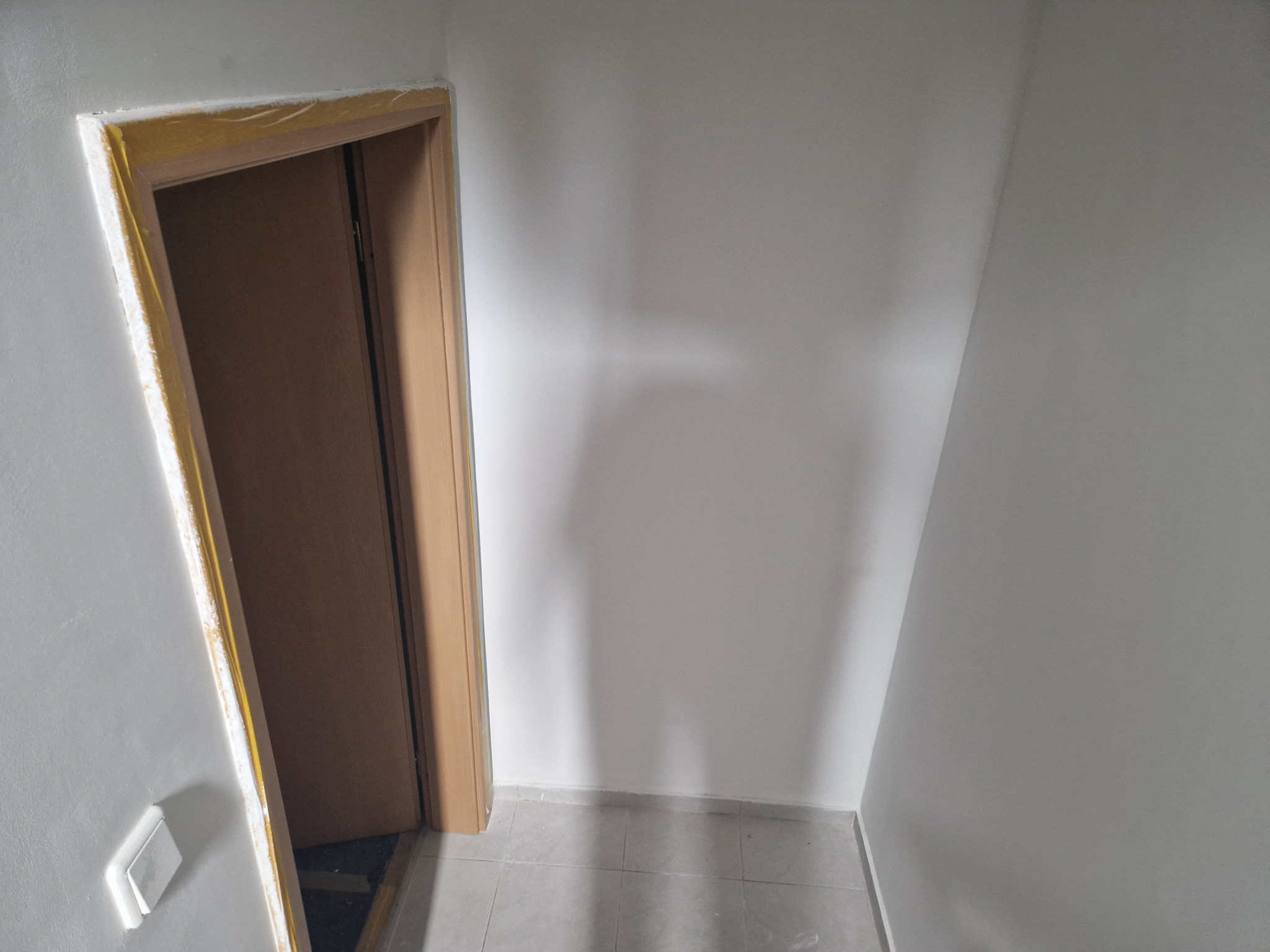 Świeżo wyszpachlowana ściana z widocznym ościeżem drzwi zabezpieczonym żółtą taśmą malarską, przygotowana do dalszych prac wykończeniowych.