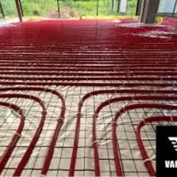 Czerwone rury ogrzewania podłogowego ułożone na siatce, zalane cienką warstwą wylewki samopoziomującej, widok z góry, surowy stan wykończenia.