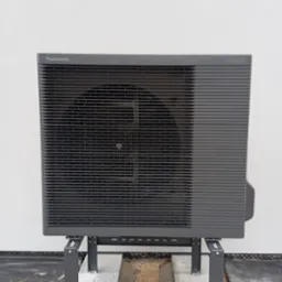 Zewnętrzna jednostka pompy ciepła Panasonic Aquarea, zamontowana na metalowym stelażu na betonowej podstawie w trakcie instalacji.