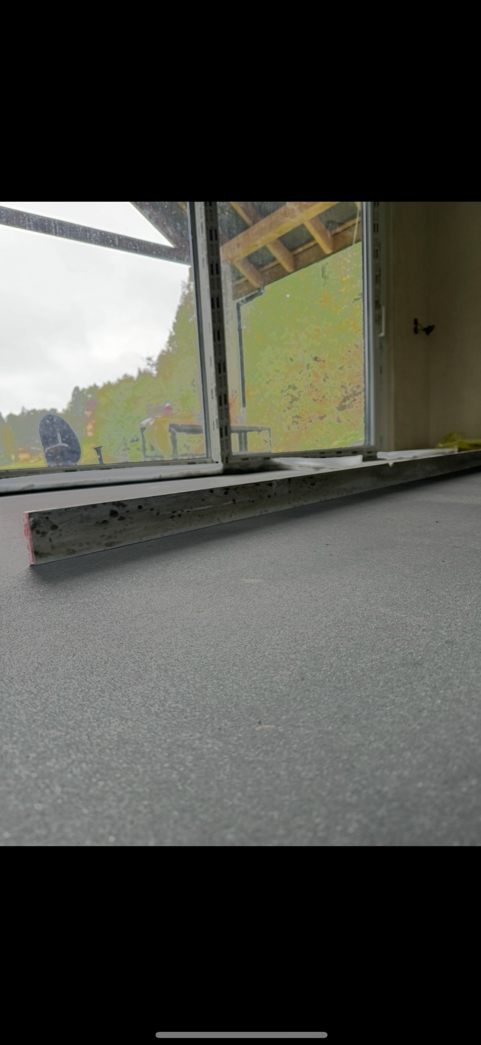 Szara, drobnoziarnista posadzka w trakcie wylewania, widoczna aluminiowa łata do rozprowadzania masy, w tle okno z widokiem na zewnątrz.