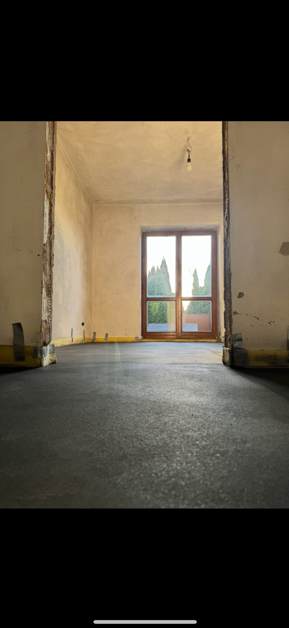 Szara wylewka samopoziomująca w jasnym pomieszczeniu z oknem, żółte listwy przypodłogowe, przygotowanie do dalszych prac wykończeniowych.