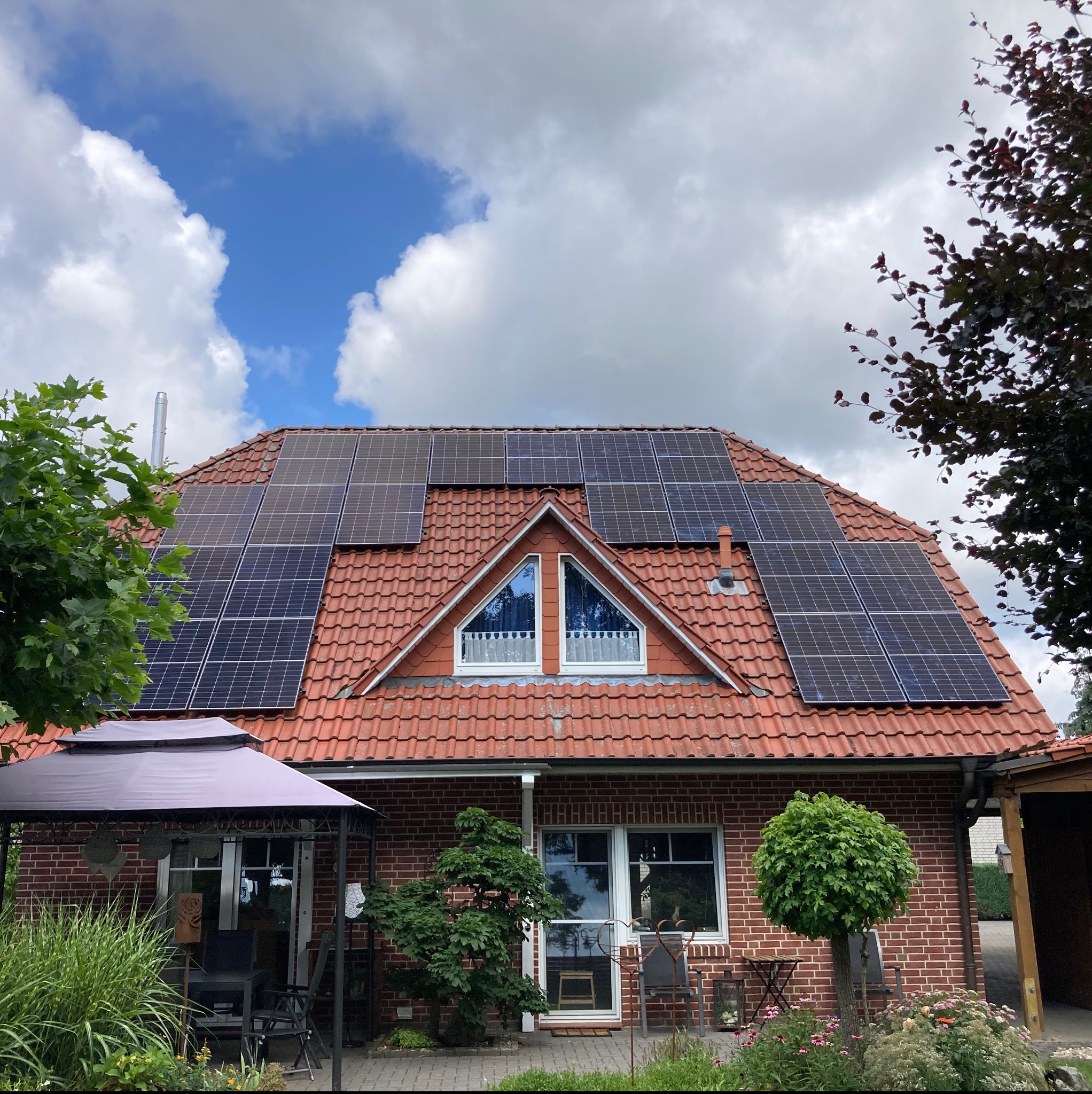 Czerwony dach domu jednorodzinnego z zainstalowanymi panelami słonecznymi, widok z poziomu ogrodu w słoneczny dzień.