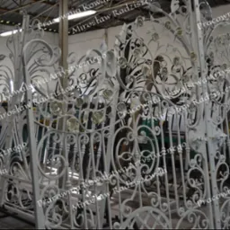 Biała, ręcznie kuta brama wjazdowa z motywem kwiatowym róży, widoczna w warsztacie przed montażem.