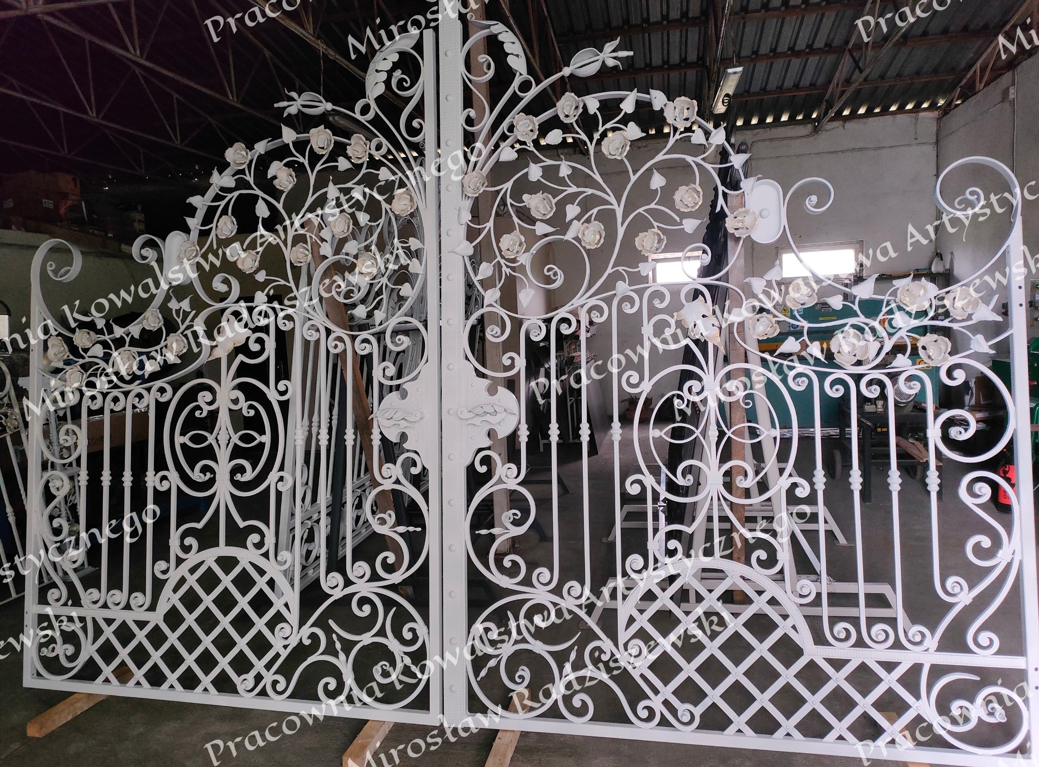 Biała, kuta brama wjazdowa z motywem roślinnym, w trakcie produkcji w warsztacie.