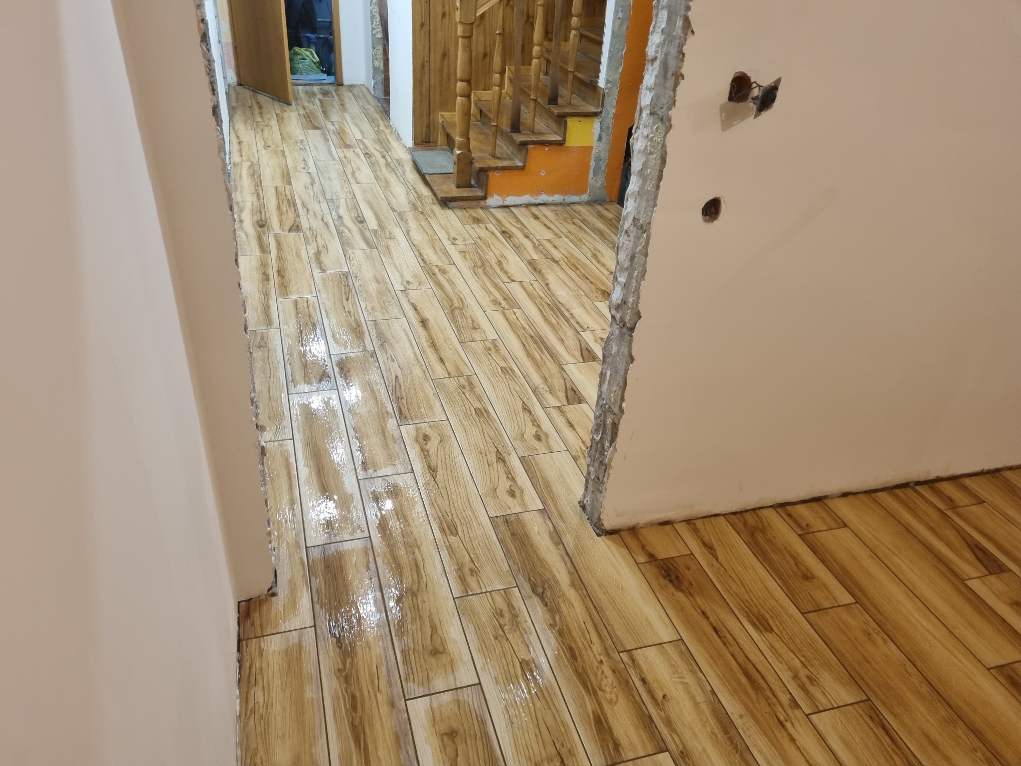 Świeżo ułożona, lśniąca podłoga z płytek imitujących drewno w korytarzu podczas remontu, widoczne schody i surowy stan wykończenia ścian