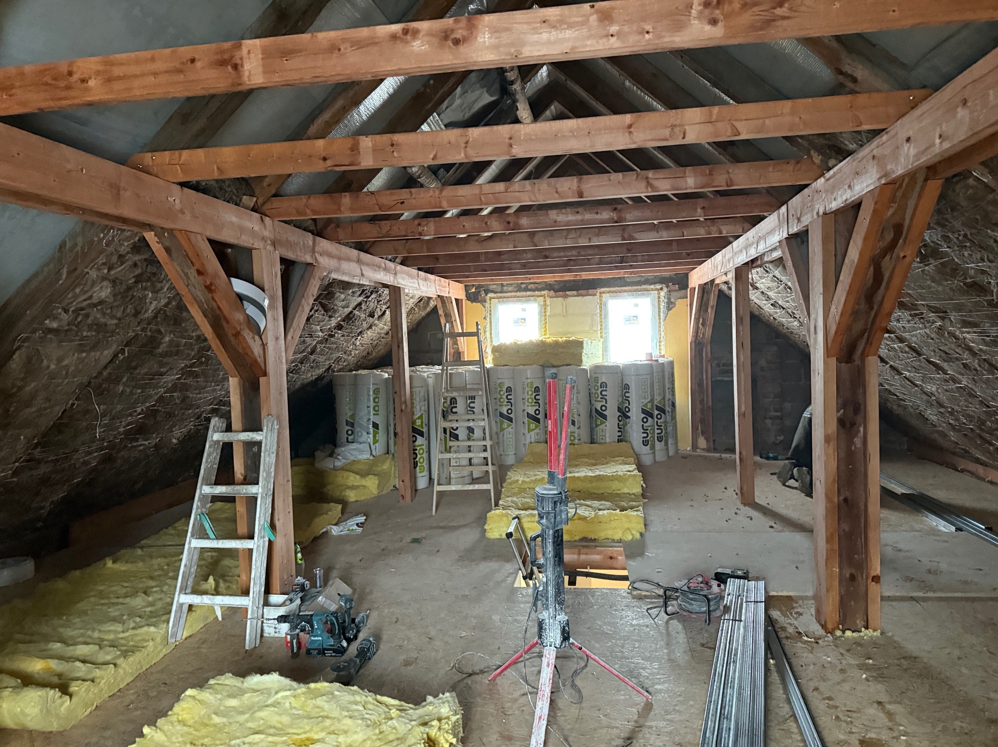 Adaptacja poddasza: drewniana konstrukcja, izolacja z wełny mineralnej w rolkach, narzędzia i profile metalowe. Etap prac wykończeniowych.