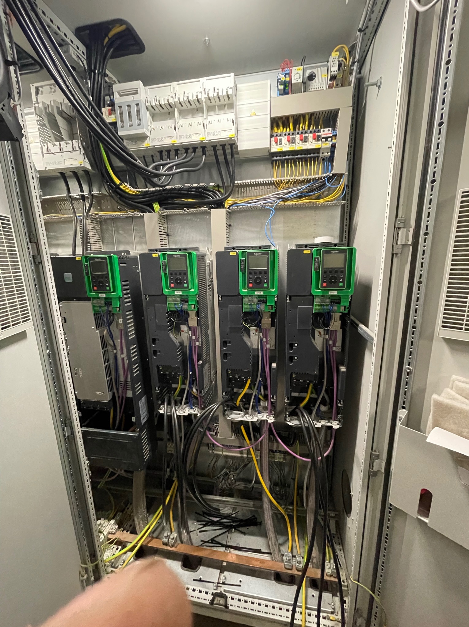 Otwarta szafa sterownicza z czterema zielonymi falownikami Schneider Electric, widoczne liczne kable i przewody, elementy montażowe i zabezpieczenia.