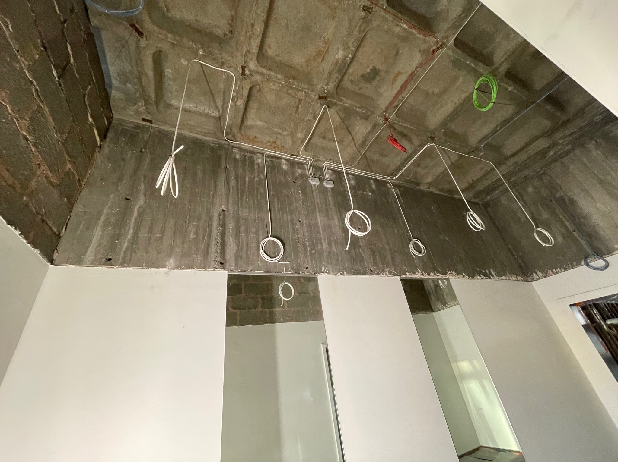 Surowy betonowy sufit z widocznymi przewodami elektrycznymi w trakcie instalacji, białe ściany w tle.