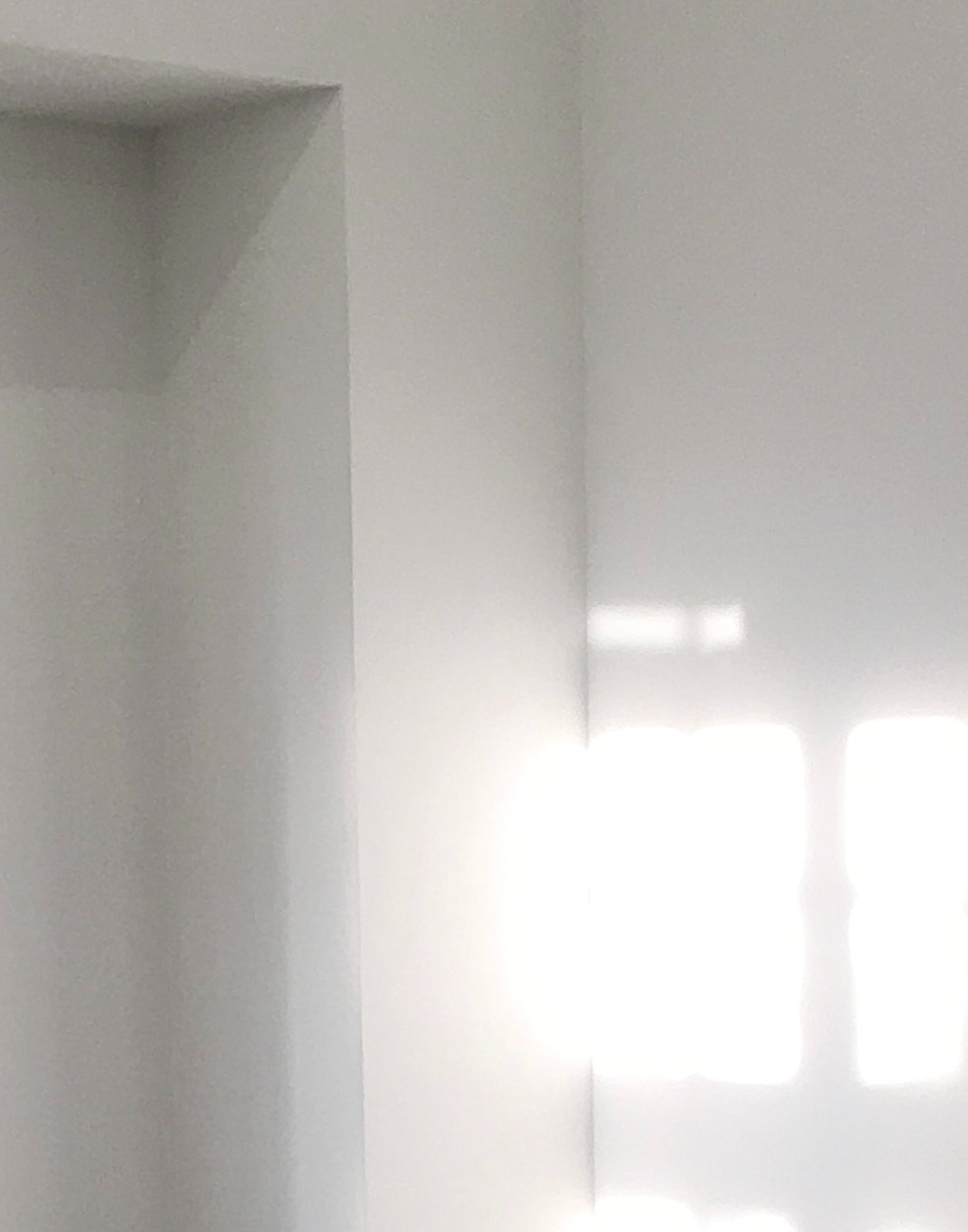 Świeżo pomalowany róg pokoju w odcieniach bieli, z widocznymi promieniami słonecznymi wpadającymi przez okno.