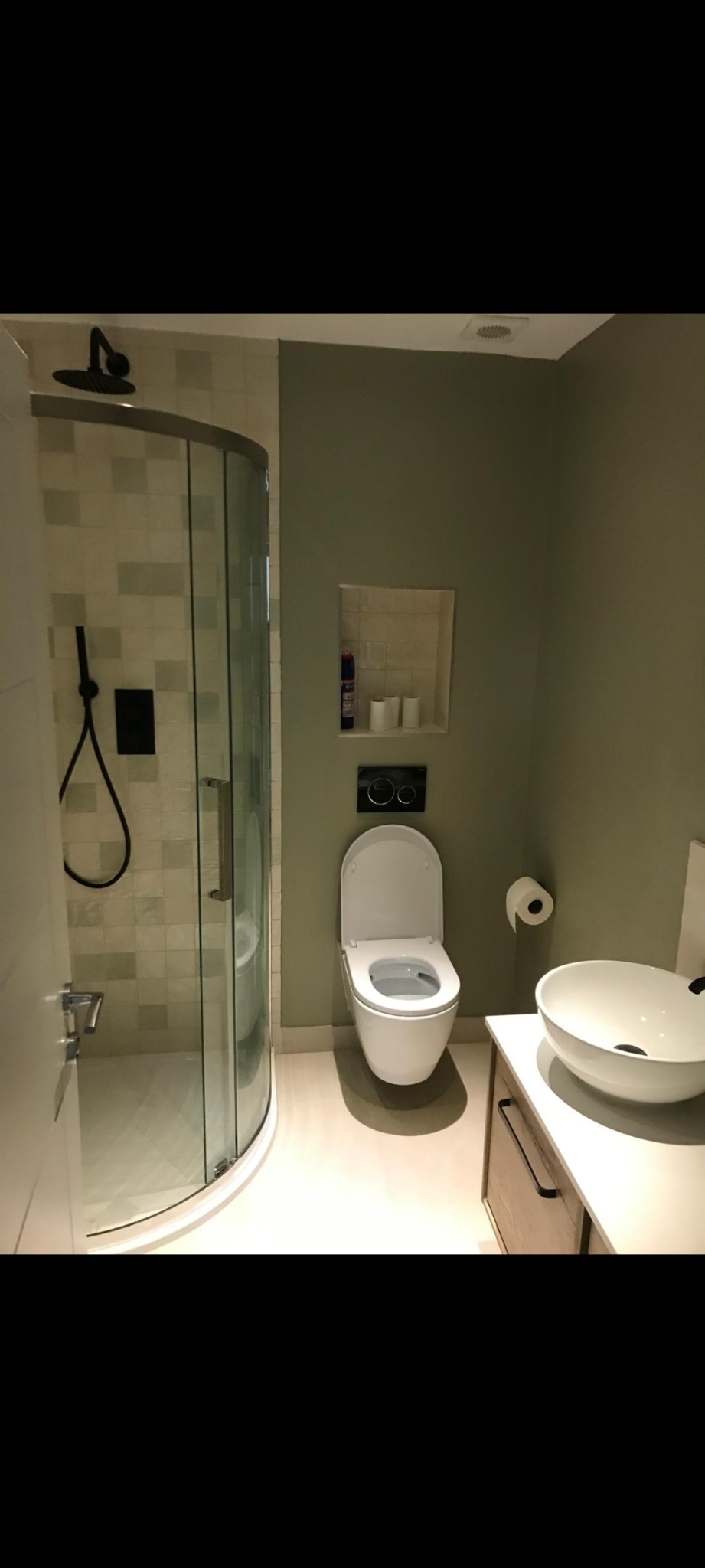 Nowoczesna łazienka z kabiną prysznicową typu walk-in, wiszącą toaletą z deską wolnoopadającą, umywalką nablatową i szafką pod umywalką w kolorze jasnego drewna, wykończona w stonowanej kolorystyce...