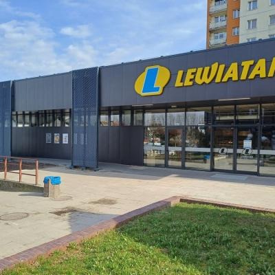 Fasada sklepu spożywczego sieci Lewiatan z szarymi panelami elewacyjnymi i dużymi, przeszklonymi drzwiami wejściowymi, widok z zewnątrz w słoneczny dzień.