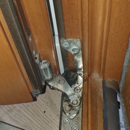 Mykola Gorganiuk Solid-Bud - Szczegółowe ujęcie mechanizmu okna drewnianego z widocznymi śrubami i elementami metalowymi, sugerujące potrzebę regulacji lub naprawy.