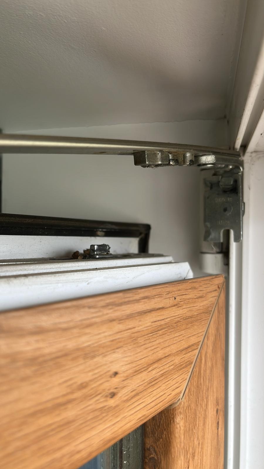 Detale mechanizmu otwierania okna PCV z drewnopodobną ramą, widoczne elementy mocujące i uszczelki.