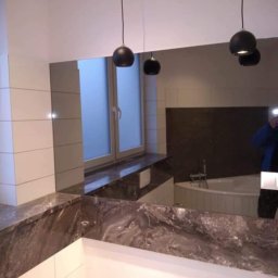 WOJT-BUD Kamil Wojtas - Nowoczesna łazienka z dużym lustrem, marmurowym blatem i wiszącymi czarnymi lampami kulami, widoczne białe płytki i okno z matową szybą.