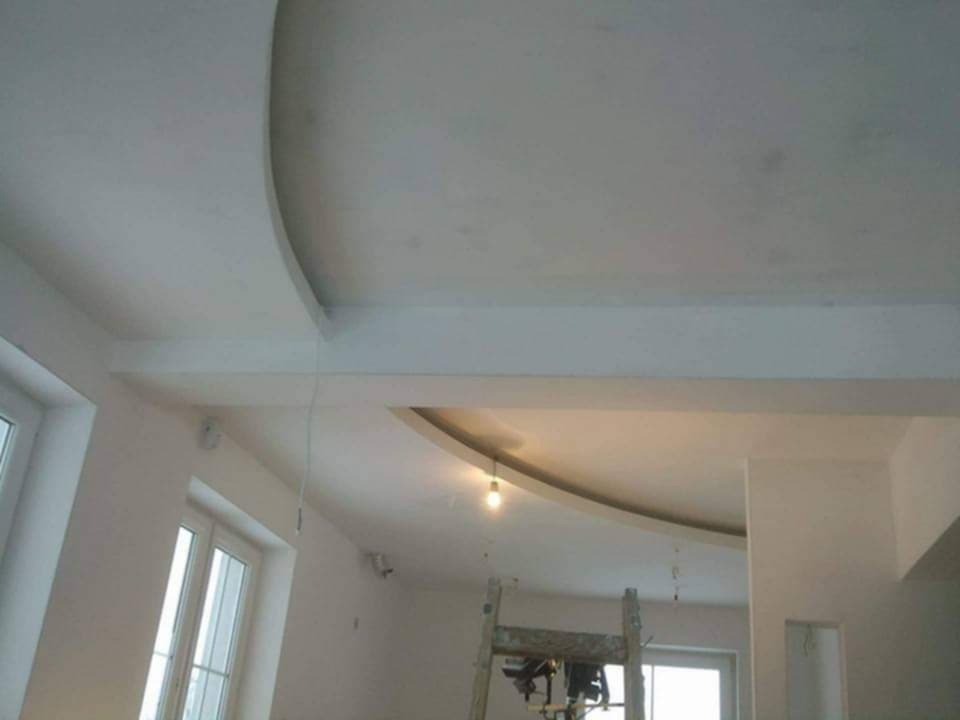 Wnętrze w trakcie prac wykończeniowych: widoczny sufit z elementami dekoracyjnymi z płyty karton-gips, drabina i lampa wisząca na kablu.