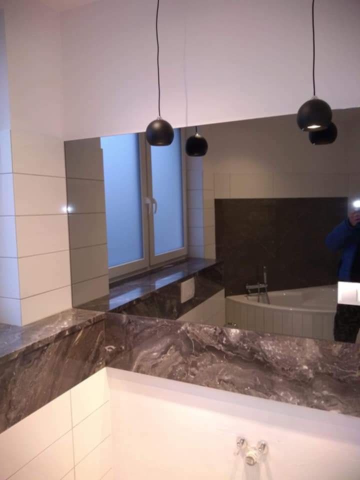 Nowoczesna łazienka z dużym lustrem, marmurowym blatem i wiszącymi czarnymi lampami kulami, widoczne białe płytki i okno z matową szybą.