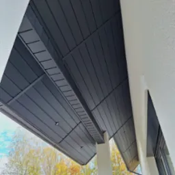 Nowoczesna zabudowa podbitki dachowej z oświetleniem punktowym, widok z dołu na tle jesiennych drzew.