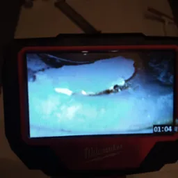 Ekran kamery inspekcyjnej marki Milwaukee wyświetla obraz z wnętrza rury, widoczny osad i zanieczyszczenia, na ekranie widoczny czas nagrania.