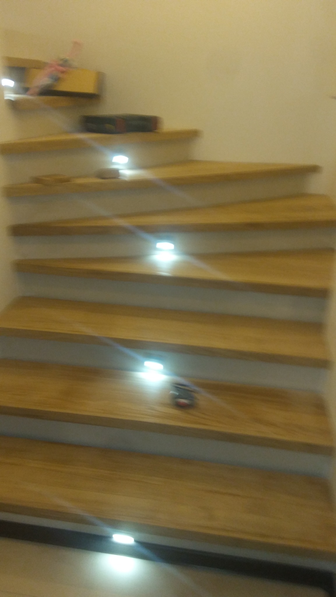 Drewniane schody z podświetleniem LED, zabawka na jednym ze stopni, widok z dołu.