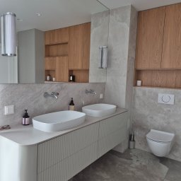 PURO Częstochowa - Nowoczesna łazienka z dwoma umywalkami nablatowymi, drewnianymi szafkami i szarą płytką imitującą kamień. Minimalistyczny design, oświetlenie punktowe i akcesoria.