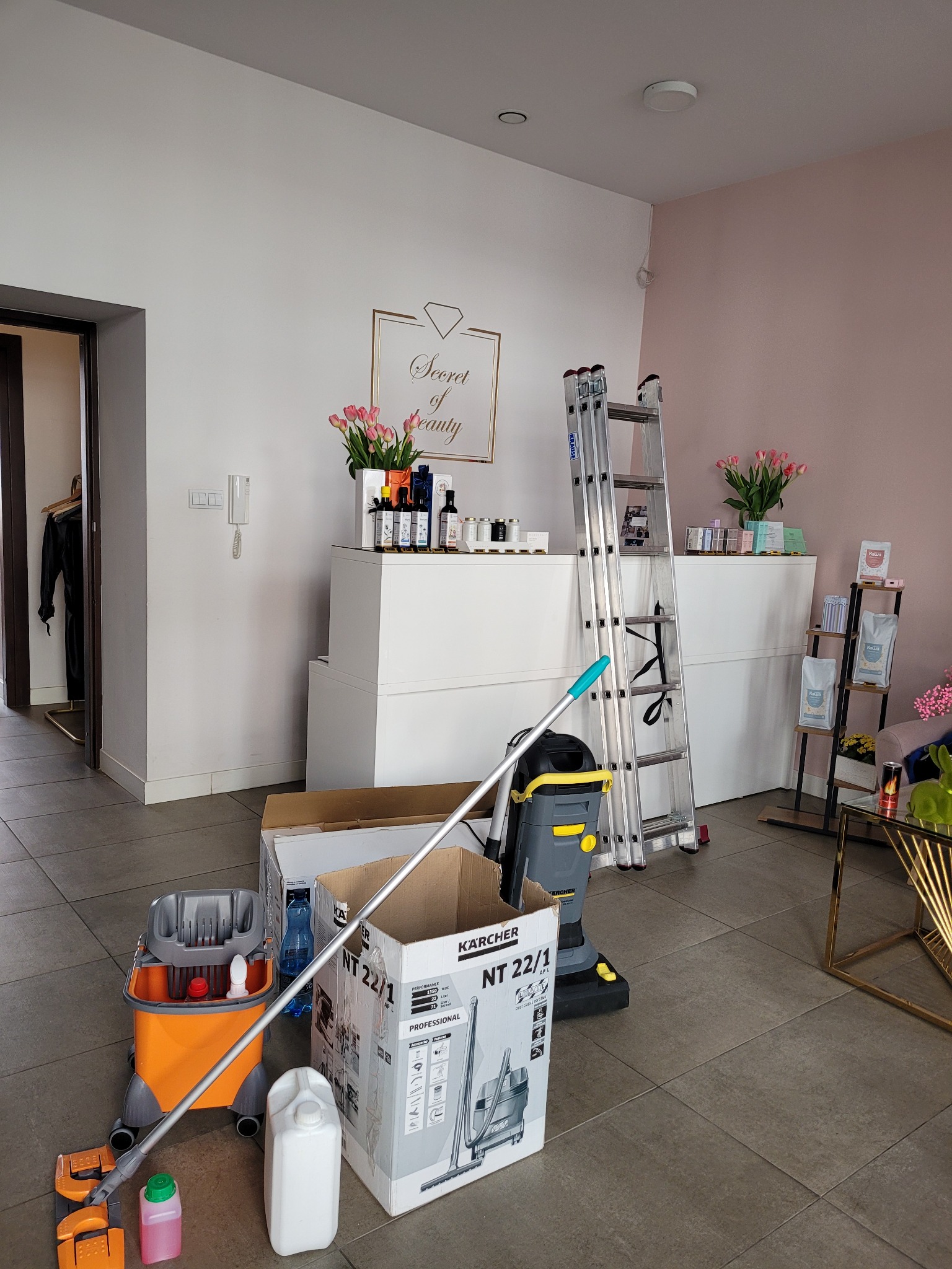 Wnętrze salonu beauty w trakcie porządkowania: drabina, odkurzacz Karcher, mop, środki czystości, karton po odkurzaczu. Przygotowania do sprzątania.