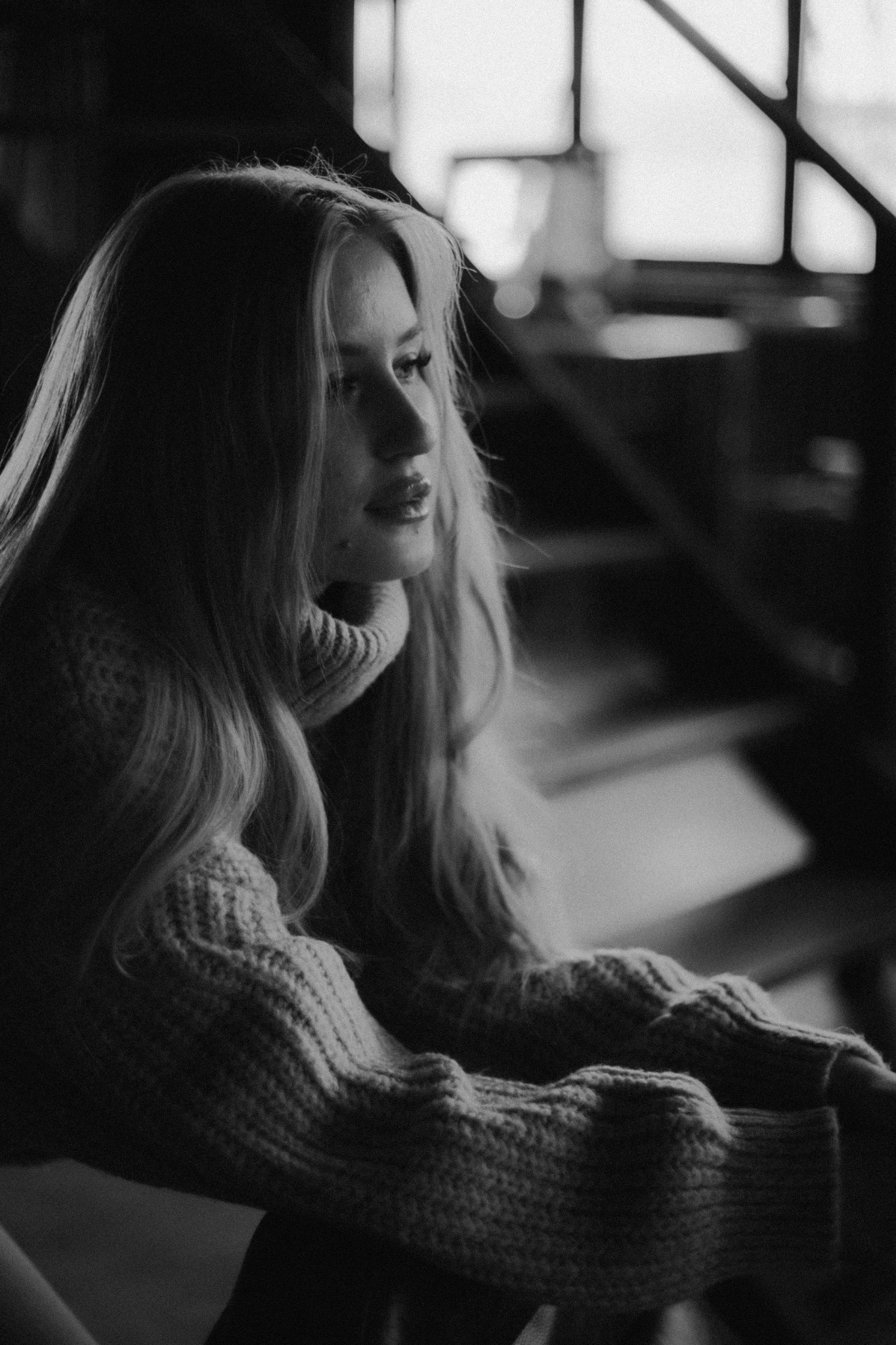 Portret młodej kobiety o długich blond włosach, ubrana w gruby, wełniany sweter z golfem, w czarno-białej tonacji, z delikatnym oświetleniem bocznym, zamyślona poza z wzrokiem skierowanym w lewo.