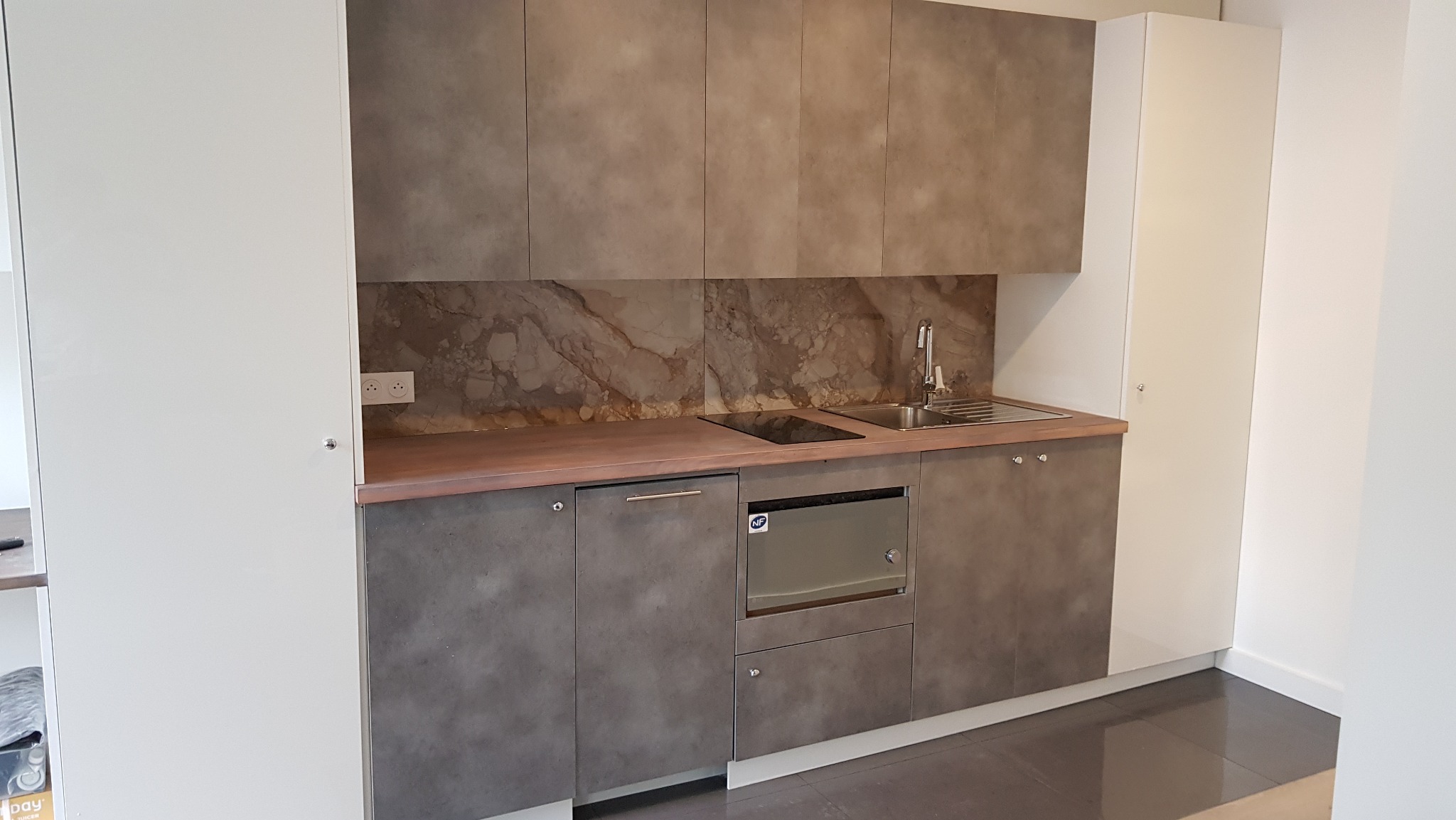 Nowoczesna kuchnia z szarymi frontami szafek, marmurowym backsplashiem i blatem w odcieniu brązu, uzupełniona białymi szafkami po bokach.