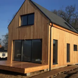 Surowy, nowoczesny dom z jasnego drewna w Tatyni, z dużym tarasem i ciemną blachą na dachu, w trakcie wykończenia.