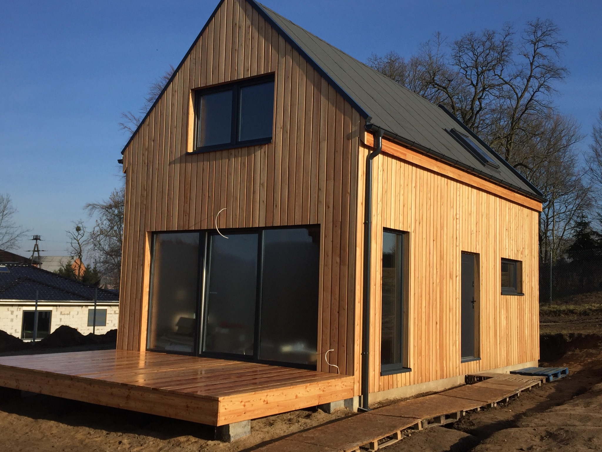 Surowy, nowoczesny dom z jasnego drewna w Tatyni, z dużym tarasem i ciemną blachą na dachu, w trakcie wykończenia.