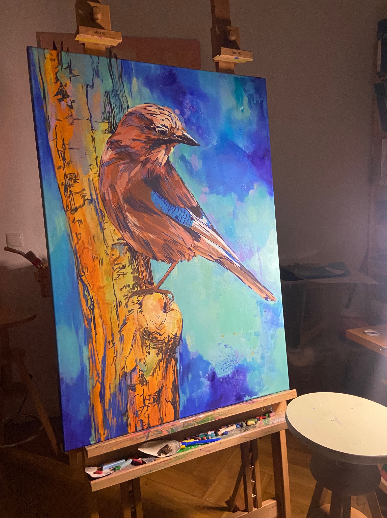 Obraz przedstawiający ptaka na drzewie, namalowany w ekspresyjnym stylu, widoczny na sztaludze w pracowni w Frankfurt (Oder).