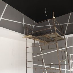 Zander Oleksandr Prishchenko - Pokój w trakcie malowania z czarnym sufitem i szarą ścianą z białymi, ukośnymi pasami, widoczne rusztowanie malarskie.