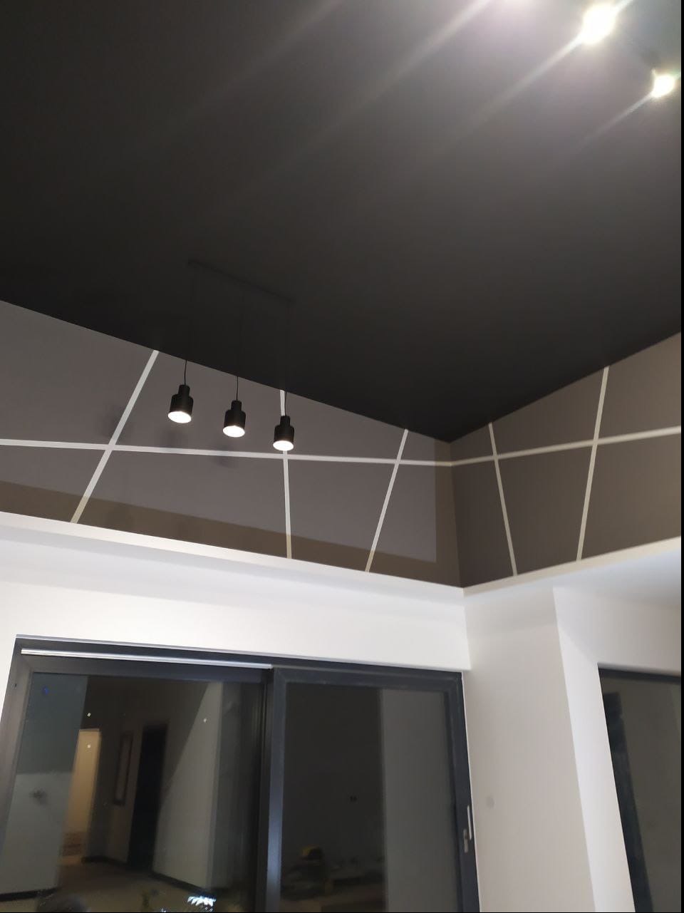 Ciemnoszary sufit z trzema wiszącymi lampami i dekoracyjnymi białymi liniami na ścianach, widok z dołu na nowocześnie wykończone wnętrze.