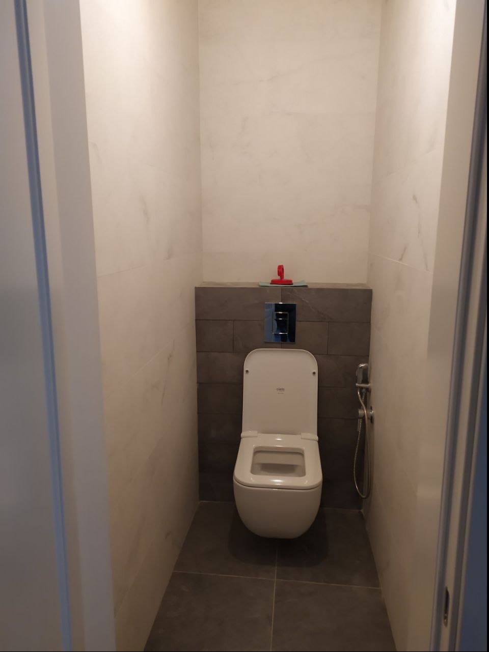 Nowoczesna toaleta z podtynkowym spłukiwaniem i bidetką w wykończonej łazience w Krakowie, z marmurowymi płytkami na ścianach i szarą mozaiką za toaletą.