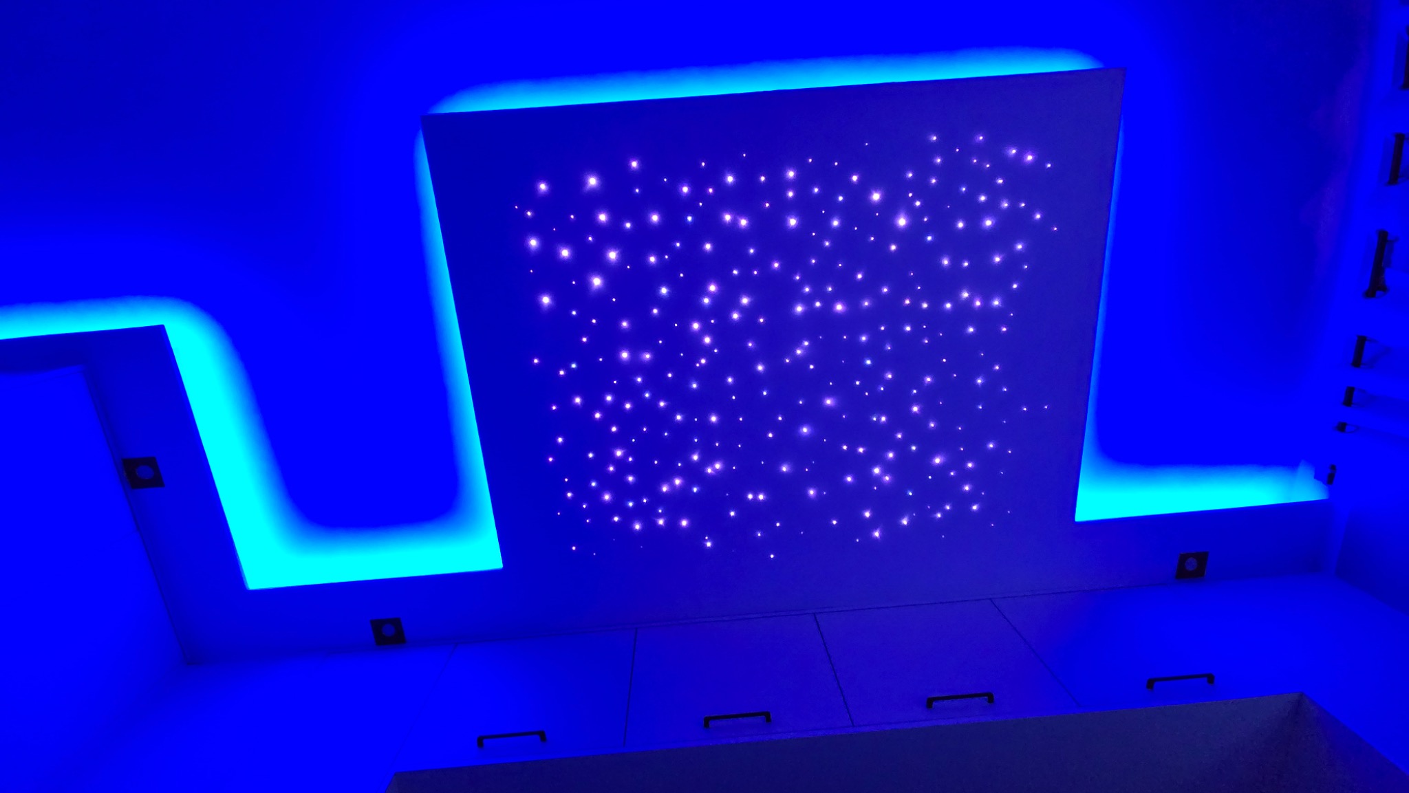 Sufit podwieszany z oświetleniem LED imitującym rozgwieżdżone niebo, otoczony niebieskim światłem obrysowym.