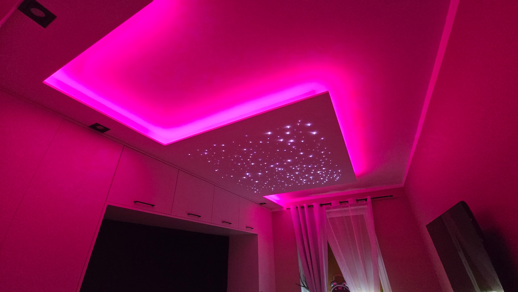Sufit podwieszany z efektem gwieździstego nieba, oświetlony różowym światłem LED, widok z dołu.