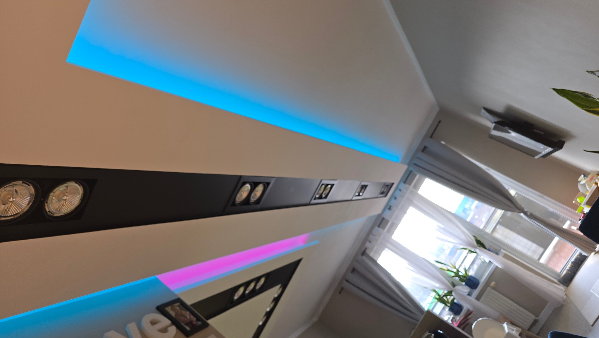 Nowoczesne oświetlenie sufitowe z podświetleniem LED w kolorze niebieskim i różowym, widok z dołu, z elementami wystroju wnętrza.