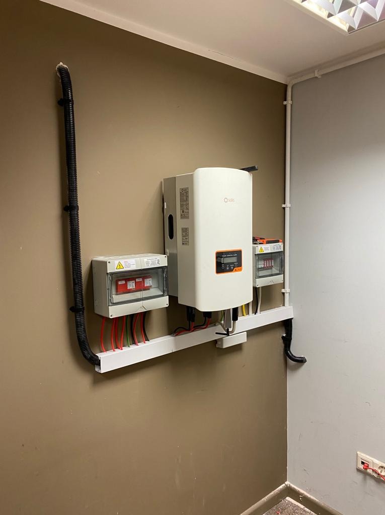 Wewnętrzna instalacja fotowoltaiczna: biały inwerter Solis, skrzynki zabezpieczające i peszel z przewodami zamocowane na ścianie w pomieszczeniu.