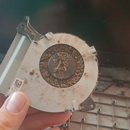 Pc_Zone - Zablokowany kurzem wentylator laptopa trzymany w dłoni, widoczne wnętrze obudowy laptopa z nagromadzonym pyłem.