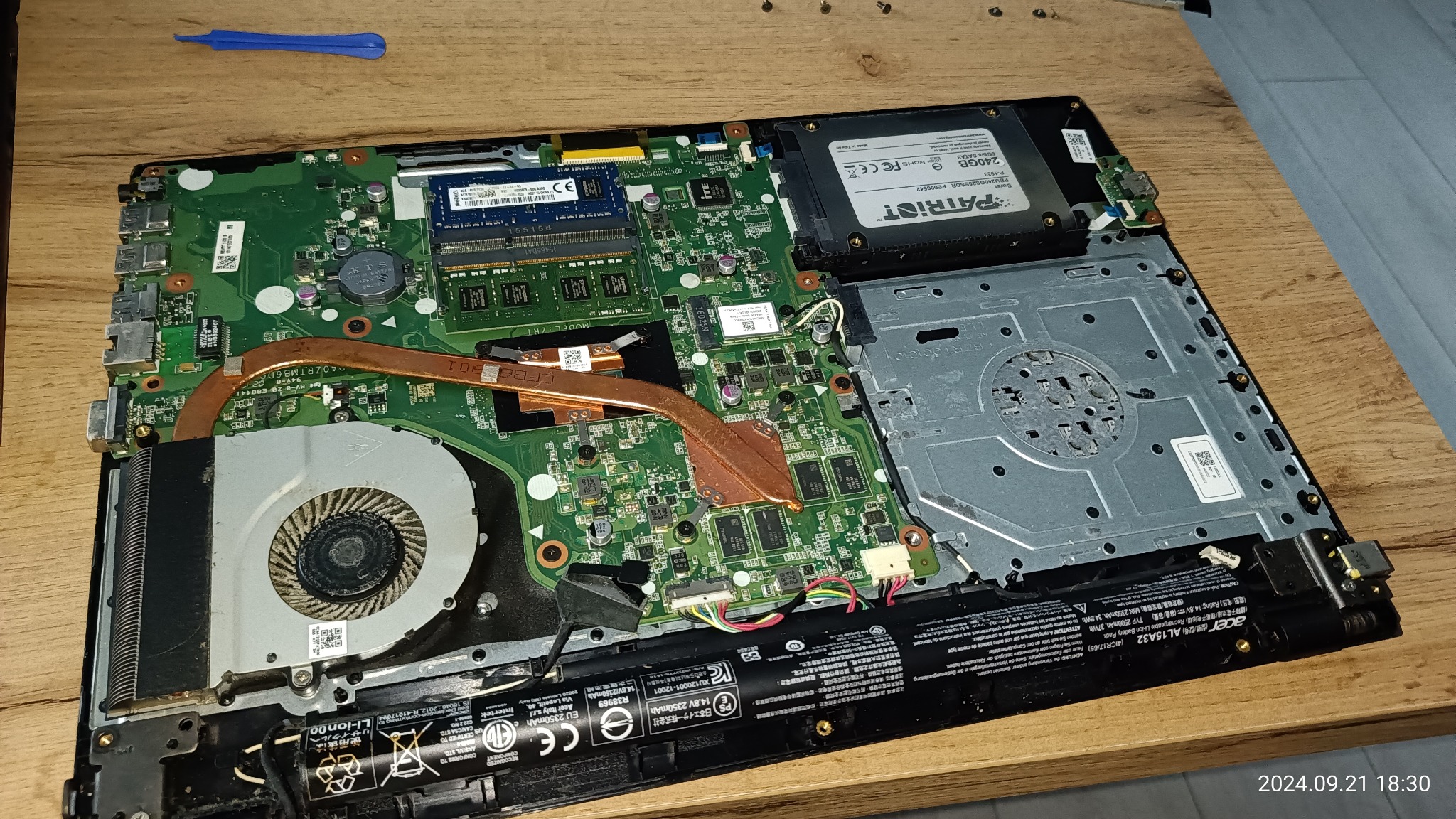 Wnętrze otwartego laptopa z widoczną płytą główną, wentylatorem, baterią i dyskiem SSD Patriot 240GB, ukazujące etap diagnozy lub naprawy.