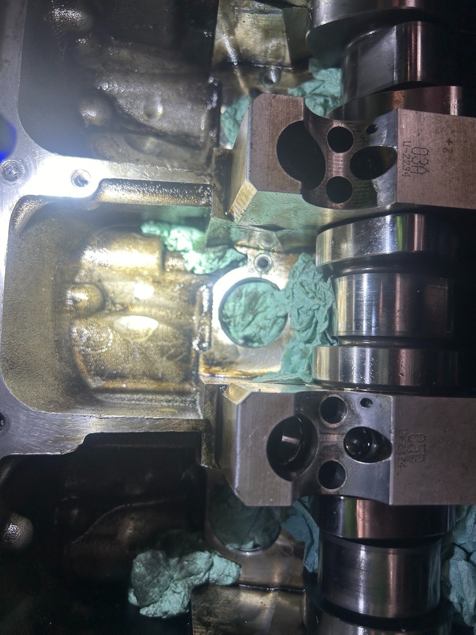 Wnętrze głowicy silnika z wałkiem rozrządu, widoczne ślady oleju i fragmenty papieru zabezpieczającego.