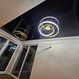 Build in Trust - Czarny, lustrzany sufit napinany z nowoczesnym, okrągłym oświetleniem LED w nowocześnie wykończonym salonie z dużymi oknami balkonowymi.