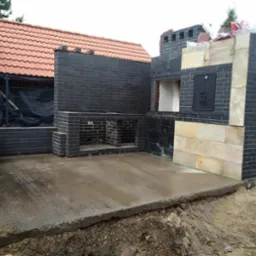 Nowo wybudowany, czarny, ceglany grill z wędzarnią i piecem chlebowym, z elementami piaskowca, na wilgotnym betonowym tarasie w Dąbrowie Górniczej.