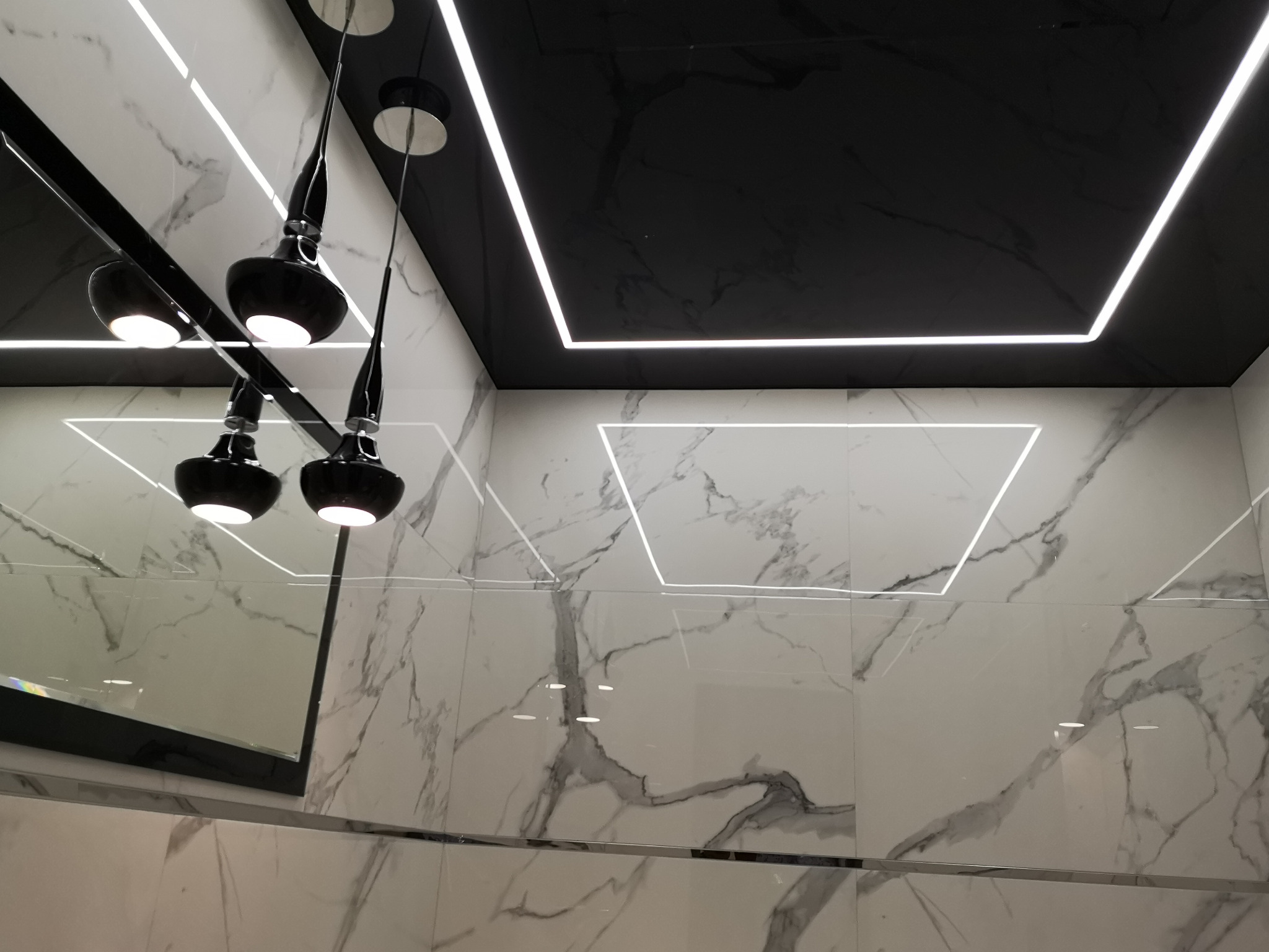 Nowoczesna łazienka z czarnym sufitem podwieszanym z oświetleniem LED, marmurowe płytki ścienne i designerskie lampy wiszące z czarnymi kloszami.