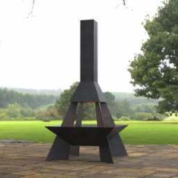 Nowoczesne palenisko ogrodowe z ciemnego metalu o geometrycznej formie, umieszczone na kamiennej posadzce z zielonym trawnikiem i drzewami w tle.