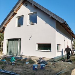 Renova Lublin - Świeżo otynkowany dom jednorodzinny w jasnych barwach, z widocznymi śladami prac wykończeniowych wokół budynku i przygotowanym sprzętem do dalszych prac na elewacji, na tle błękitnego nieba.