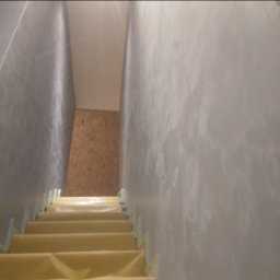 Renova Lublin - Klatka schodowa w trakcie prac wykończeniowych; schody zabezpieczone folią ochronną, ściany pokryte jasnoszarą, dekoracyjną strukturą imitującą marmur.