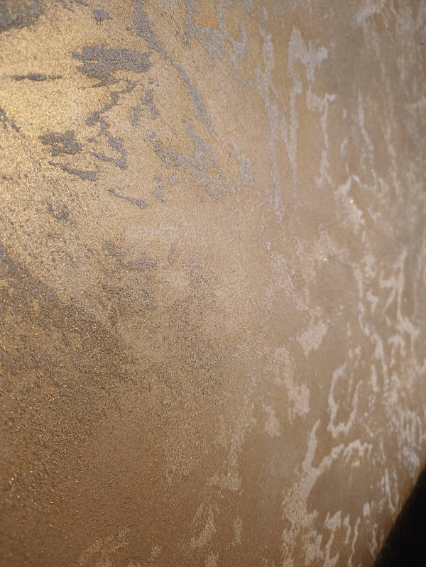 Dekoracyjna ściana z efektem metalicznego złota i srebrnych przetarć, wykonana techniką imitującą naturalny kamień.