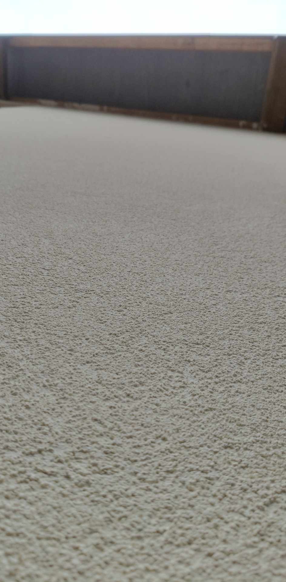 Jasna ściana z fakturą baranka, widoczna z dołu, z fragmentem ciemniejszego elementu konstrukcyjnego u góry.