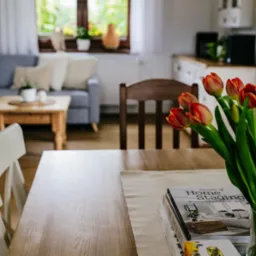 St&oacute;ł z bukietem tulipan&oacute;w i książkami o home stagingu w jasnym wnętrzu w Bielsku-Białej. W tle widoczny szary narożnik.