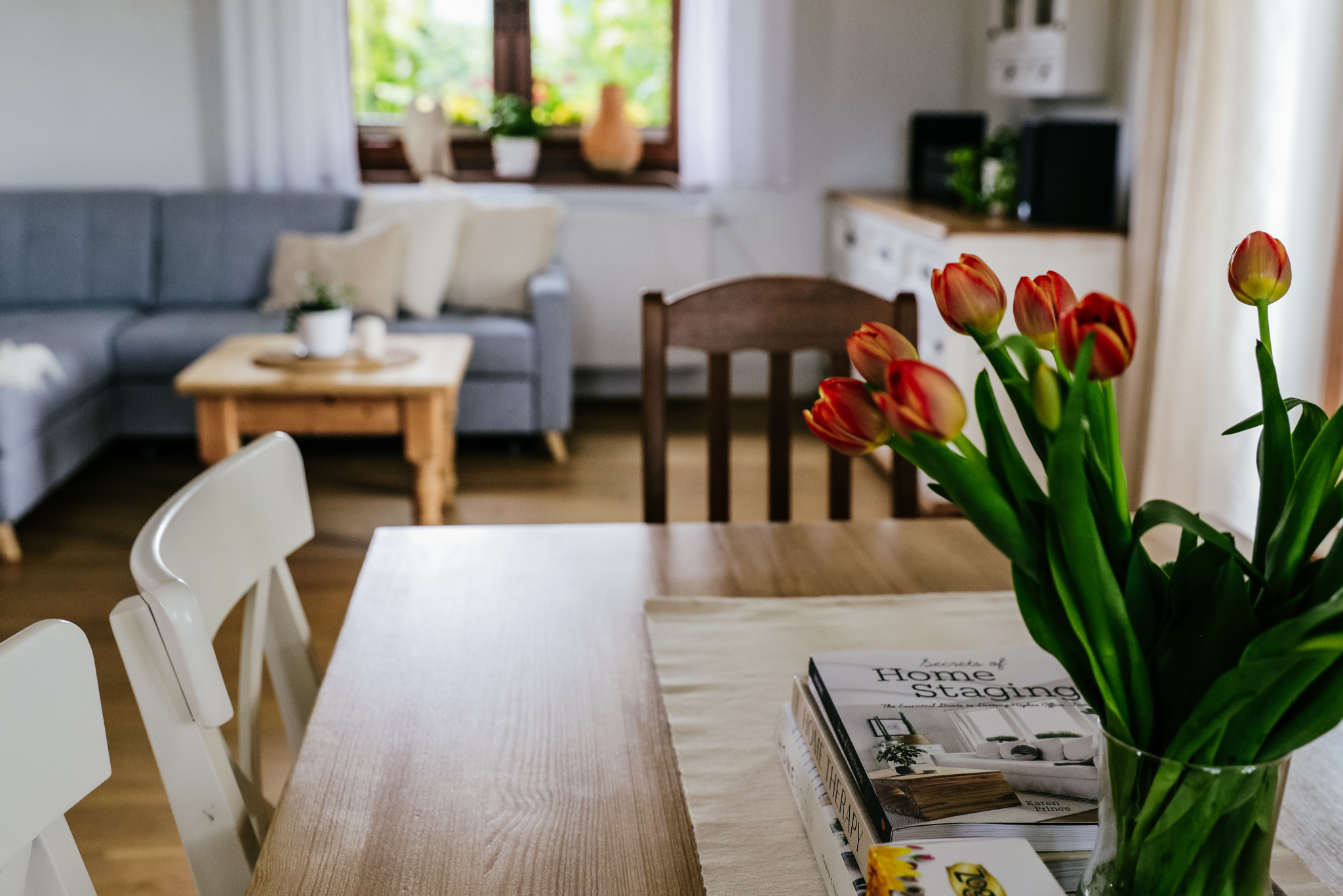 Stół z bukietem tulipanów i książkami o home stagingu w jasnym wnętrzu w Bielsku-Białej. W tle widoczny szary narożnik.